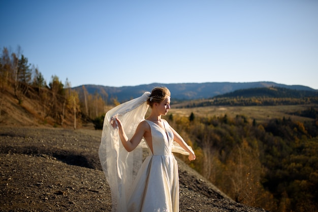 Retrato de uma jovem noiva linda nas montanhas com um véu. O vento desenvolve um véu. Fotografia de casamento nas montanhas.