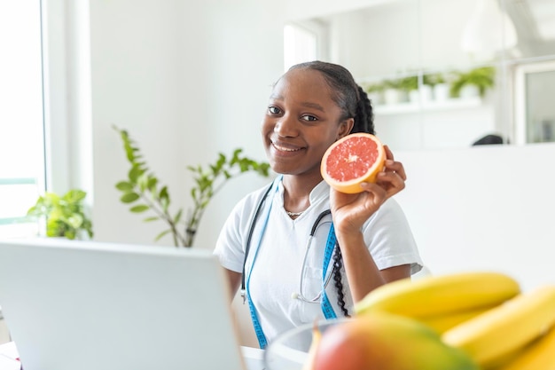 Foto retrato de uma jovem nutricionista sorridente na sala de consulta. mesa de nutricionista com suco de frutas saudável e fita métrica. dietista trabalhando em um plano de dieta.