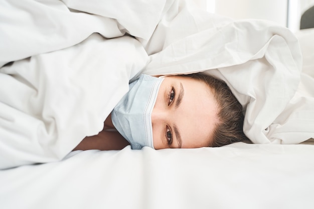 Retrato de uma jovem paciente do sexo feminino, branca, com uma máscara facial descartável, cuidando da cama