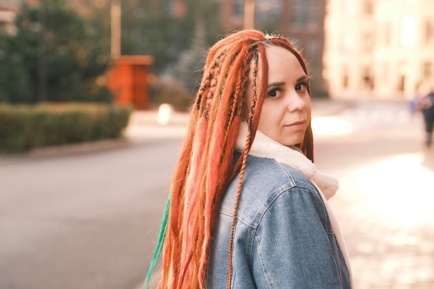 Retrato de uma jovem positiva com dreadlocks na rua da cidade moderna Muito feminina com penteado brilhante olhando para longe sorrindo