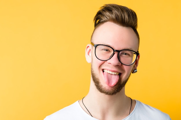 Retrato de uma jovem positiva e alegre com um pente na moda sobre o corte de cabelo. Homem engraçado e emocional mostrando a língua.