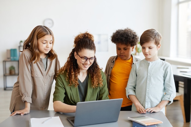 Retrato de uma jovem professora usando computador com diversos grupos de crianças