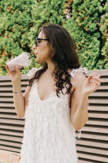 Retrato de uma jovem que bebe um coquetel refrescante em um dia quente de verão Um modelo em um elegante vestido branco e óculos de sol