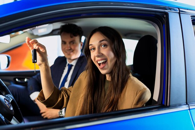 Retrato de uma jovem que está sentada no carro com a chave do carro Um consultor de vendas está sentado no banco do passageiro Comprando um carro novo em uma concessionária