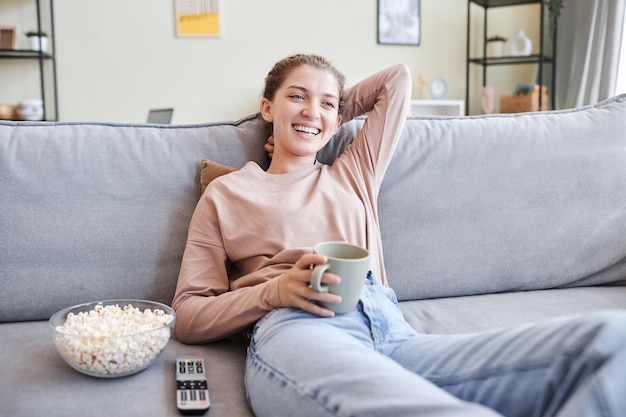 Retrato de uma jovem relaxada vendo TV em casa e rindo no espaço de cópia