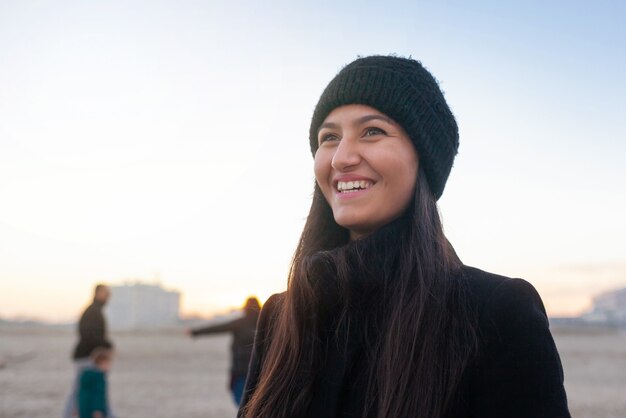 Retrato de uma jovem rindo na praia com roupas de inverno.