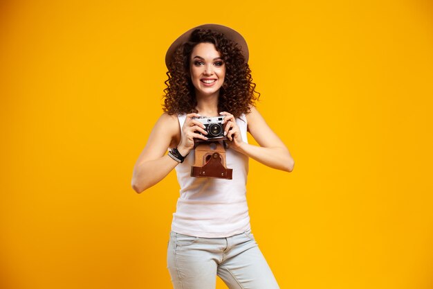 Retrato de uma jovem rindo tirando fotos em uma câmera fotográfica vintage retrô isolada em amarelo brilhante