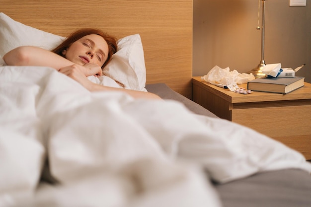 Retrato de uma jovem ruiva calma e doente, vestindo roupas noturnas macias, dormindo em uma cama confortável, deitada em um travesseiro macio
