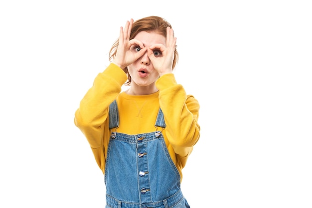 Retrato de uma jovem ruiva fazendo máscara de óculos com dedos fazendo caretas isoladas em fundo branco