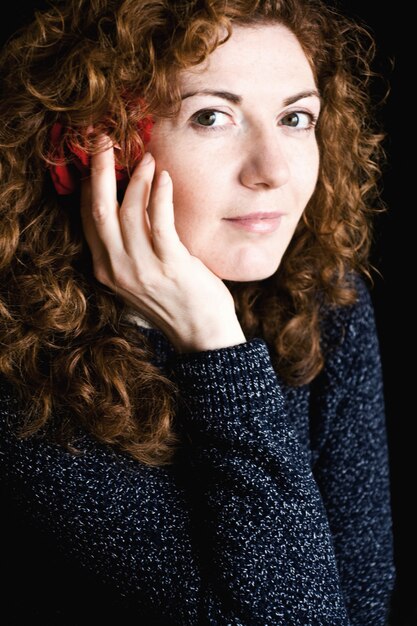 Retrato de uma jovem ruiva linda com uma rosa vermelha encaracolada no cabelo em um escuro