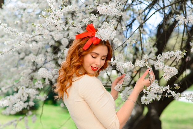 Retrato de uma jovem ruiva linda em um vestido branco com flores da primavera