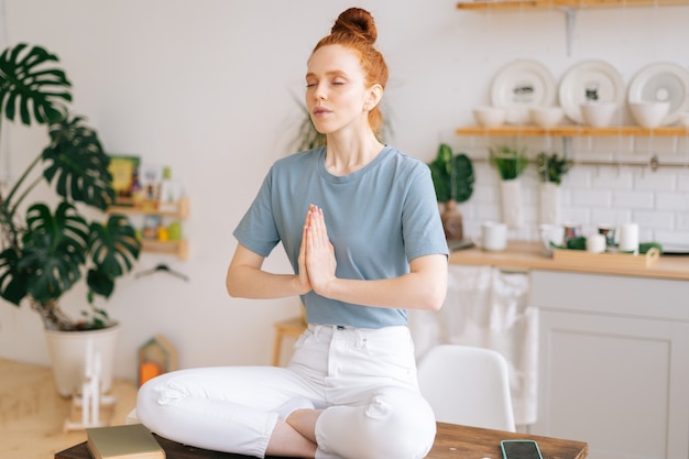 Retrato de uma jovem ruiva meditando em paz e juntando as mãos