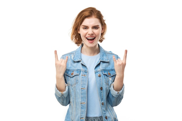 Retrato de uma jovem ruiva mostrando gesto de rock and roll com os dedos isolados no fundo branco