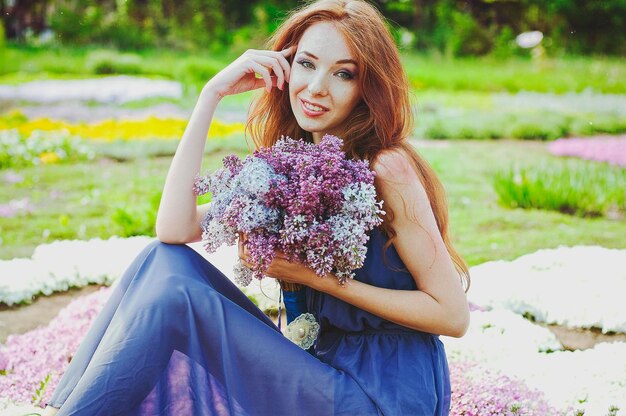 Retrato de uma jovem ruiva no jardim primavera. sardas. florescendo flores roxas. buquê de lilases