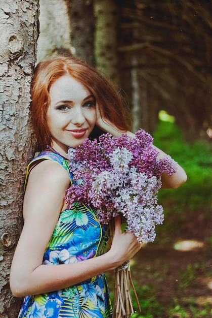 Retrato de uma jovem ruiva no jardim primavera. sardas. florescendo flores roxas. buquê de lilases