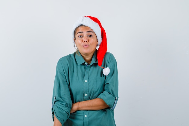 Retrato de uma jovem segurando a mão na barriga com uma camisa, chapéu de Papai Noel e olhando surpresa para a frente