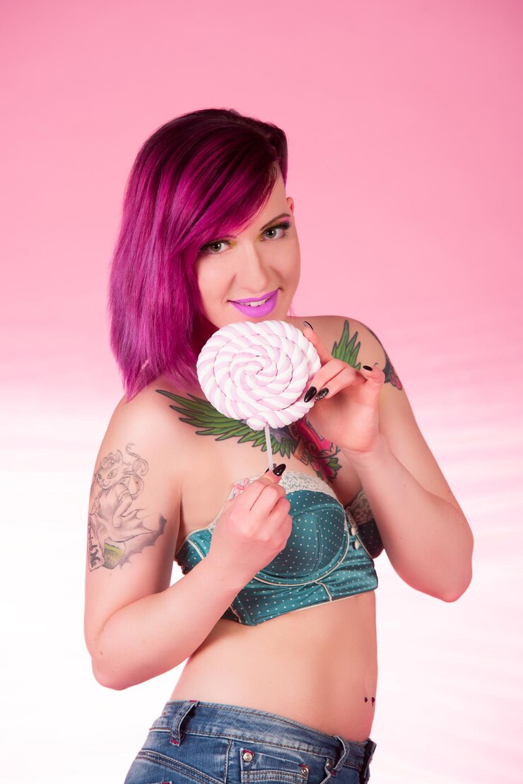 Foto retrato de uma jovem segurando um pirulito enquanto está de pé contra um fundo rosa