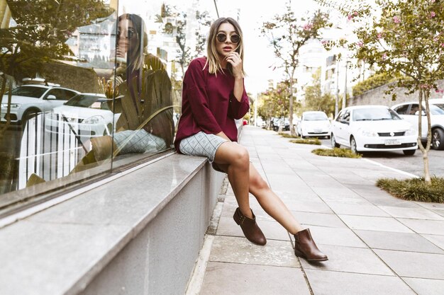 Foto retrato de uma jovem sentada na calçada de um edifício de vidro