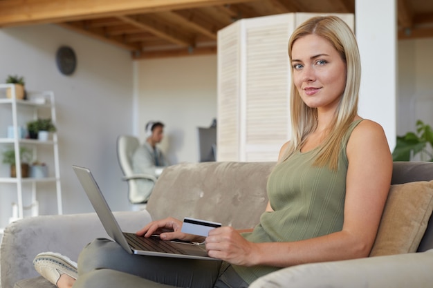 Retrato de uma jovem sentada no sofá com um laptop e trabalhando online na sala de estar em casa