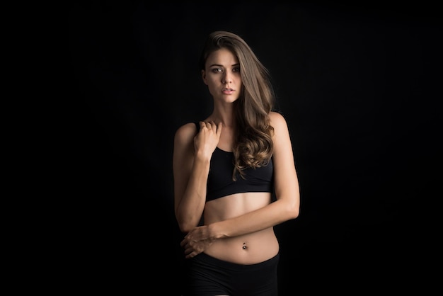 Retrato de uma jovem séria vestindo lingerie em pé contra um fundo preto