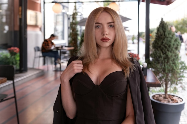 Retrato de uma jovem sexy com cabelos loiros e terno preto com decote de coração no café olha para a câmera