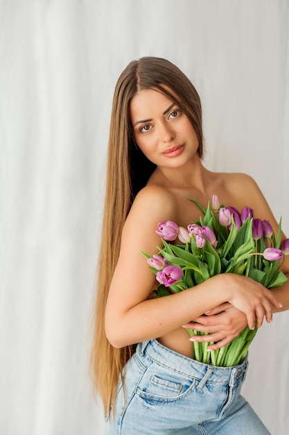 Retrato de uma jovem sexy e bonita com modelo de cabelo comprido com um buquê de tulipas lilás em feriados de primavera brancos