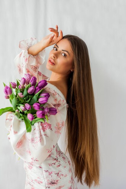 Retrato de uma jovem sexy e bonita com modelo de cabelo comprido com um buquê de tulipas lilás em feriados de primavera brancos