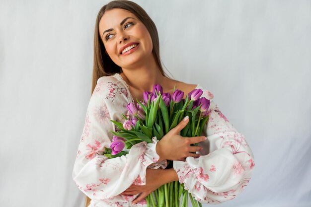 Retrato de uma jovem sexy e bonita com modelo de cabelo comprido com um buquê de tulipas lilás em feriados de primavera brancos