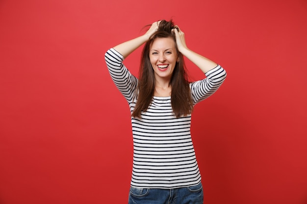 Retrato de uma jovem sorridente alegre em roupas listradas casuais em pé colocando as mãos na cabeça