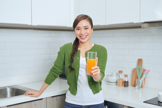 Retrato de uma jovem sorridente bebendo suco de laranja na cozinha de casa