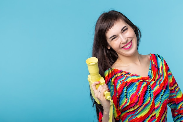 Retrato de uma jovem sorridente com uma câmera de vídeo vintage amarela nas mãos, posando