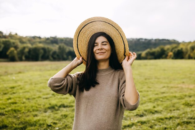 Retrato de uma jovem sorridente desfrutando do bom tempo usando um chapéu de palha ao ar livre em um campo