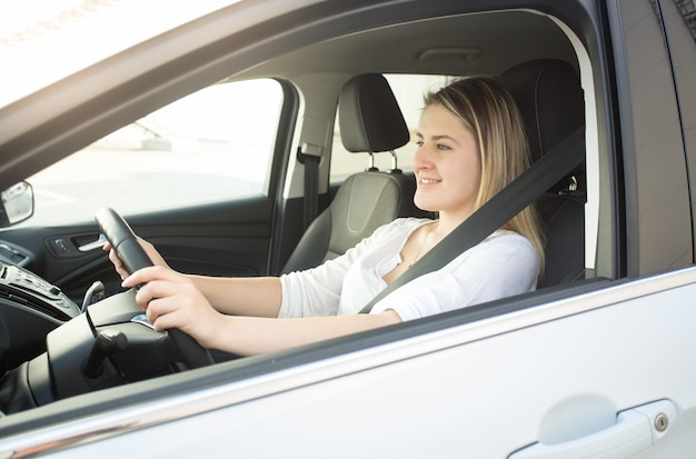 Retrato de uma jovem sorridente, dirigindo um carro e olhando para a estrada