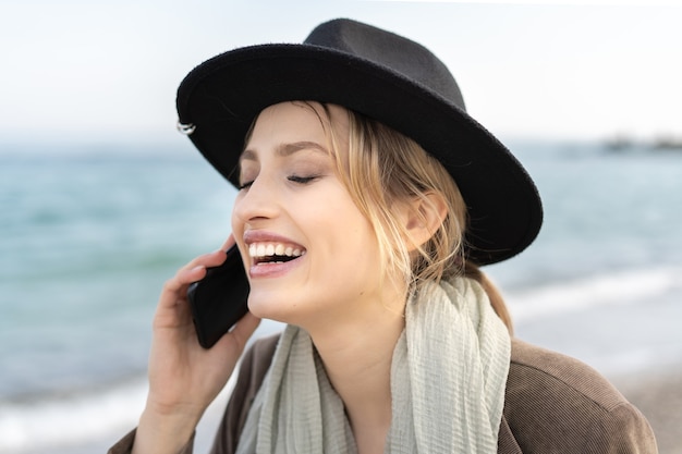 Retrato de uma jovem sorridente e alegre falando em seu telefone celular e rindo com um chapéu estiloso