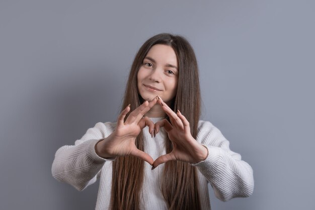 Retrato de uma jovem sorridente e atraente mostrando um gesto de coração com as duas mãos