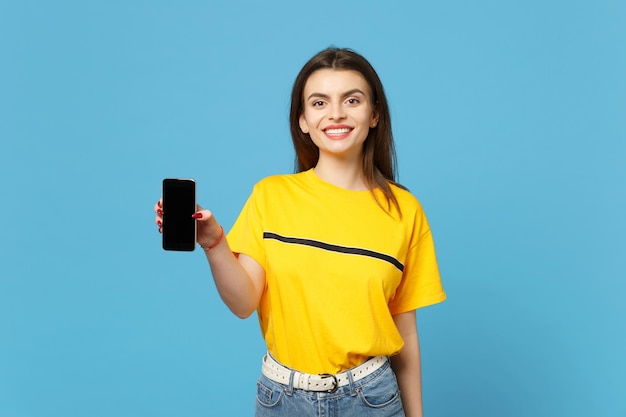 Retrato de uma jovem sorridente em roupas casuais vívidas, segurando o celular com tela vazia em branco isolada no fundo da parede azul brilhante no estúdio. conceito de estilo de vida de pessoas. mock up espaço de cópia.