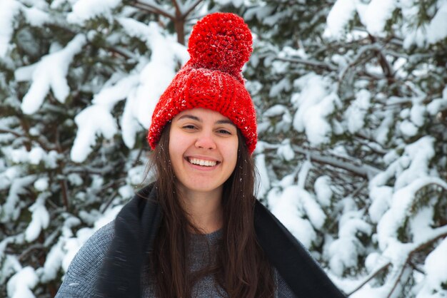 Retrato de uma jovem sorridente em roupas de inverno com chapéu vermelho com árvore de abeto bubo no fundo