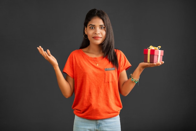 Retrato de uma jovem sorridente feliz segurando a caixa de presente em um fundo cinza