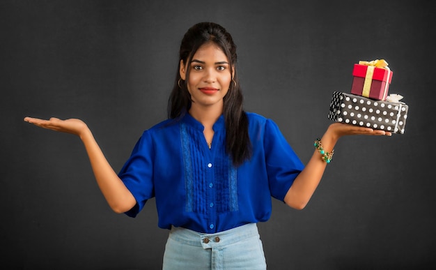 Retrato de uma jovem sorridente feliz segurando a caixa de presente em um fundo cinza