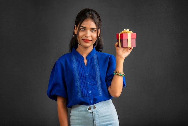 Retrato de uma jovem sorridente feliz segurando a caixa de presente em um fundo cinza
