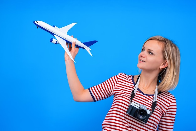 Retrato de uma jovem sorridente loira feliz com roupas listradas de verão com uma câmera segurando o avião