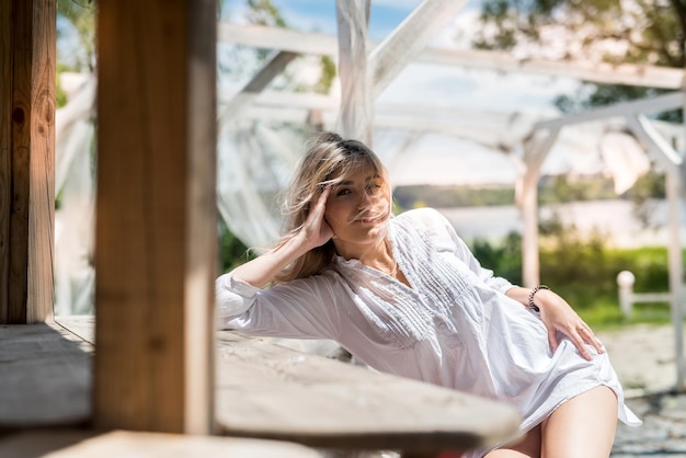 Retrato de uma jovem sorridente que aproveita o tempo de férias, perto da praia de areia no gazebo de madeira.