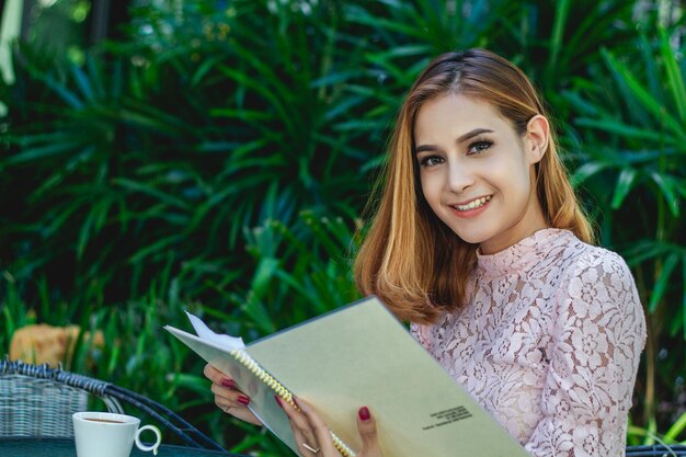 Foto retrato de uma jovem sorridente segurando um menu enquanto estava sentada contra as plantas