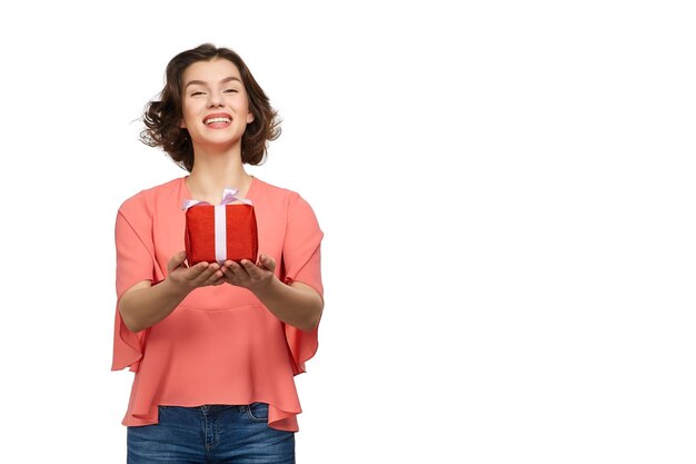 Foto retrato de uma jovem sorridente segurando um presente enquanto está de pé sobre um fundo branco