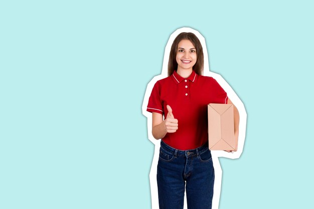 Foto retrato de uma jovem sorridente segurando uma caixa de papelão enquanto está de pé contra um fundo azul