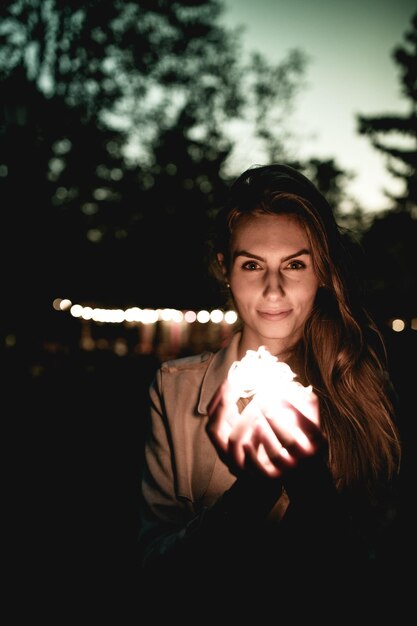 Foto retrato de uma jovem sorridente segurando uma luz iluminada à noite