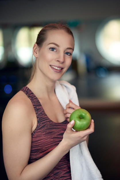 Foto retrato de uma jovem sorridente segurando uma maçã enquanto está de pé no ginásio