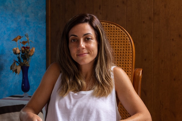 Foto retrato de uma jovem sorridente, sentada em uma poltrona com um fundo de madeira.