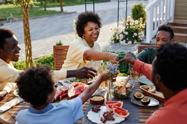 Retrato de uma jovem sorridente tilintando óculos com a família e amigos enquanto desfruta do jantar fora