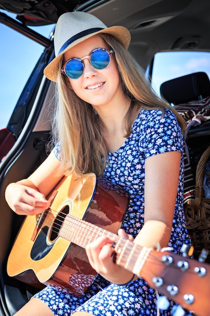 Retrato de uma jovem sorridente tocando guitarra no carro